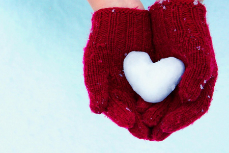 red mittens holding snow heart