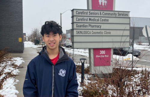 teenage boy standing in front of sign for medical facilities